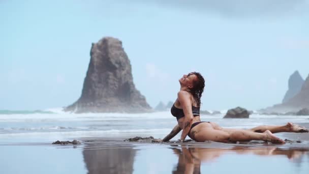 Schöne Frau im Badeanzug tanzt am Strand mit schwarzem Sand in der Nähe der Kanarischen Inseln Teneriffa — Stockvideo