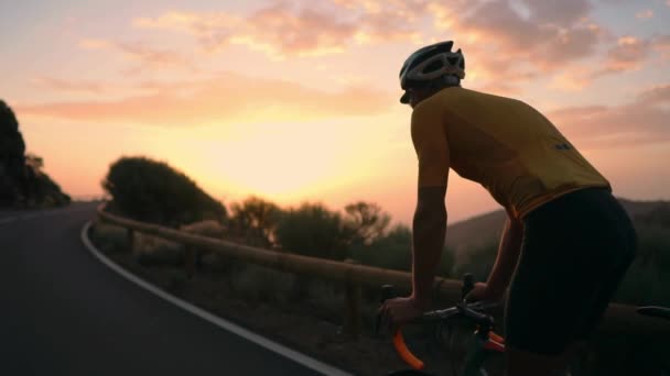 A young sports man riding a bike on a mountain serpentine in a yellow t-shirt helmet and sports equipment rear view . Slow motion steadicam — Stock Video