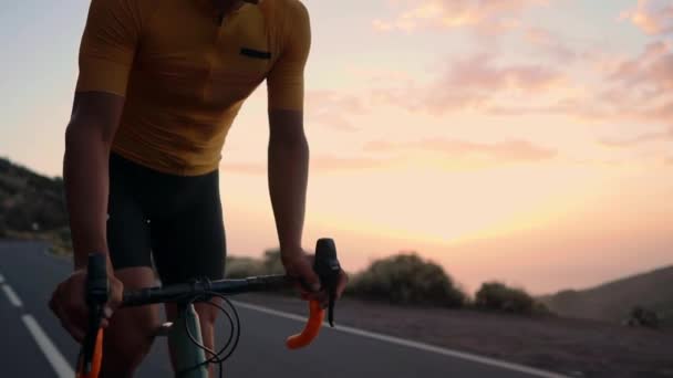 Un giovane sportivo guida una bicicletta su una serpentina di montagna e guarda la macchina fotografica con una t-shirt gialla e attrezzature sportive. Rallentatore steadicam — Video Stock