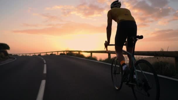 Um jovem desportista andando de bicicleta em uma montanha serpentina em um capacete amarelo t-shirt e equipamentos esportivos vista traseira. Steadicam em câmara lenta — Vídeo de Stock