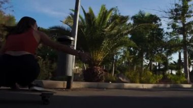 Şort ve spor ayakkabısı palmiye ağaçlarında yakınındaki bir longboard sürme yaz aylarında genç bir kadın.