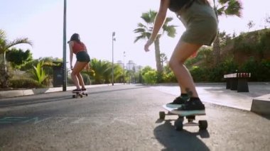 İki kadın arkadaş kaykaylar sürmek yokuş aşağı resort taşıma ve gülümseyen eğleniyor. Yol boyunca palmiye ağaçları