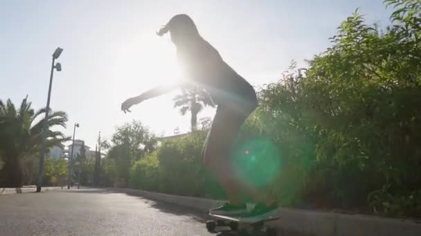 Dos chicas cabalgan al atardecer sonriendo con tablas para patinar Junta a lo largo del camino en el Parque con palmeras y arena. Vida sana personas felices — Vídeo de stock