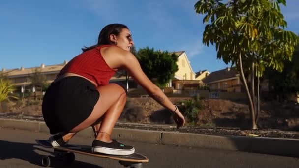 Молодая женщина летом катается на длинной доске возле пальм в шортах и кроссовках — стоковое видео