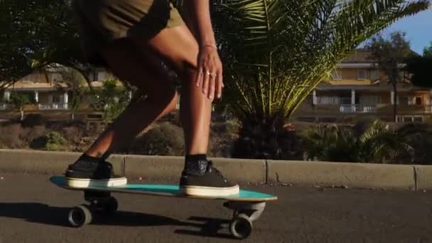 Uma jovem no verão montando um longboard perto das palmeiras em shorts e tênis — Vídeo de Stock