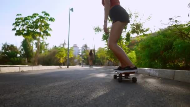 Vrouw rijden bij zonsondergang glimlachend met planken voor skate Board langs het pad in het Park met palmbomen en zand. Gezonde levensstijl gelukkige mensen — Stockvideo