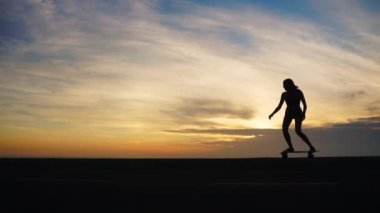 Bir kız şort ve spor ayakkabısı silüeti yolun karşı dağlar ve okyanus boyunca kaykay.