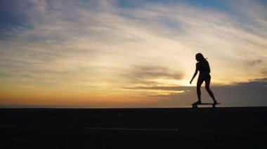 Yakın çekim siluet kaykaylar ağır çekimde günbatımı gökyüzü karşı. Kaykay yakın çekim ayakları.