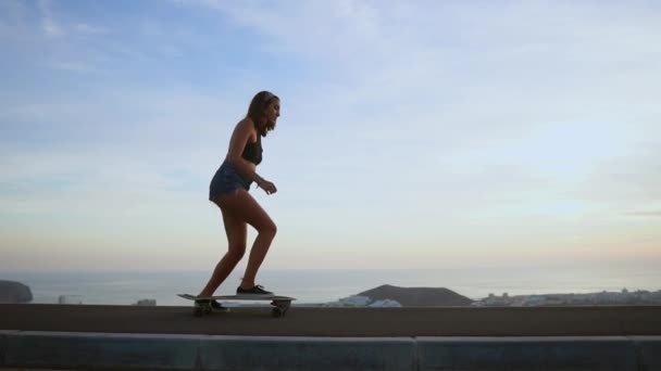 Chica montando un monopatín cerca del océano y una gran montaña en cámara lenta . — Vídeo de stock