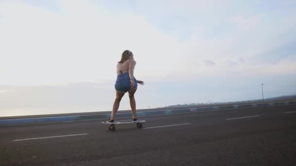 Dívka na koni skateboard nedaleko oceánu a velké hory ve zpomaleném filmu. Zdravý životní styl, sport. — Stock video