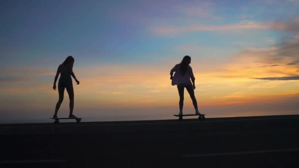 Silhouette di due ragazze che cavalcano skateboard sullo sfondo dell'oceano e del cielo al tramonto — Video Stock