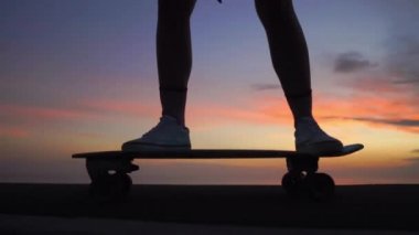 Güzel kız günbatımı gökyüzü karşı yolda bir kaykay sürmek. yakın çekim