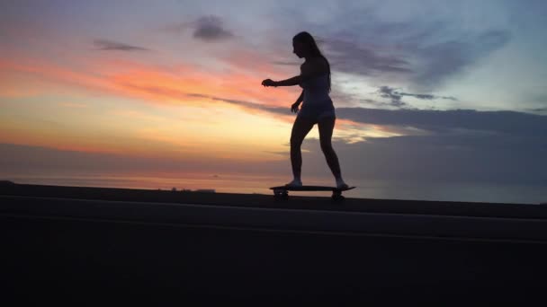 Menina bonita monta um skate na estrada contra o céu por do sol — Vídeo de Stock