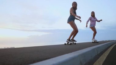 Kız skeytbordistka gitmek için gülümseyen ve okyanus ve yavaşlatılmış dağlarda arka plan üzerinde gülüyor dağlar ateş kısa şort gün batımında