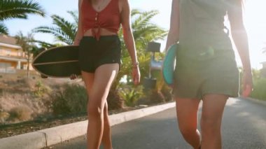 Yakın çekim Genç kadınların ellerinde kaykaylar taşımak ve bir gülümseme ile iletişim kurmak. Güneşin elinde binme panoları.