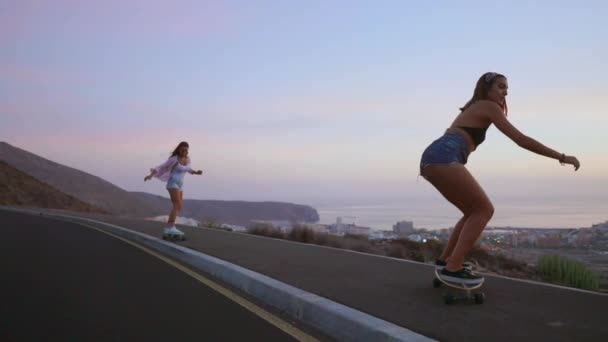 Novia skeytbordistka ir a las montañas sonriendo y riendo en el fondo del océano y las montañas en el lento rodaje en pantalones cortos al atardecer — Vídeo de stock