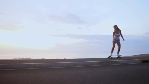 Mujer skateboarder paseos en un tablero en la pendiente contra el cielo desde la montaña — Vídeo de stock