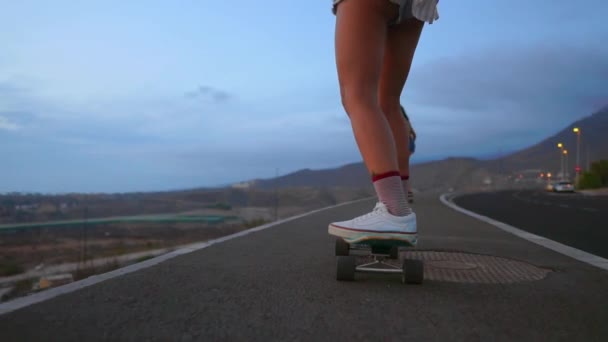 Mulher skatista passeios em uma placa na encosta contra o céu a partir da montanha — Vídeo de Stock