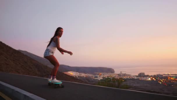Vacker flicka rider en skateboard på vägen mot solnedgång himlen — Stockvideo