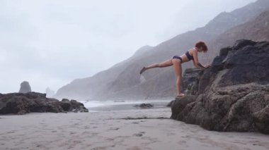 Bacağında bir taş üzerine eğilerek ağız kavgası yapıyor çok güzel bir yer spor yapan volkanik kum plaj ince zhenina