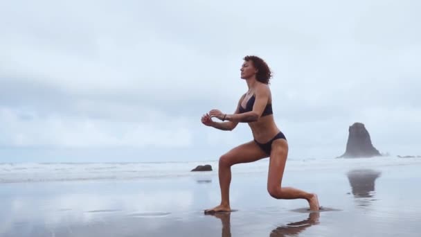 En smal kvinna nära havet gå på vattensporter att utföra utfall på varje ben. Övningar för lårmuskler i slow motion — Stockvideo