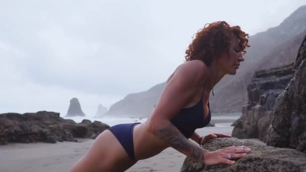 Κορίτσι αθλητής εκτελεί συμπίεση από το βράχο κατά τη διάρκεια της κατάρτισης σε μια όμορφη παραλία. — Αρχείο Βίντεο
