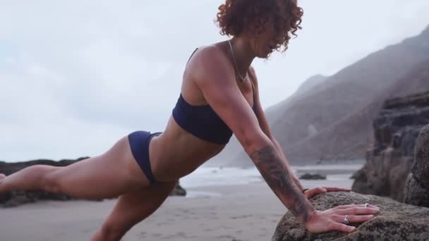 Chica atleta realiza presionar desde la roca durante el entrenamiento en una hermosa playa . — Vídeo de stock