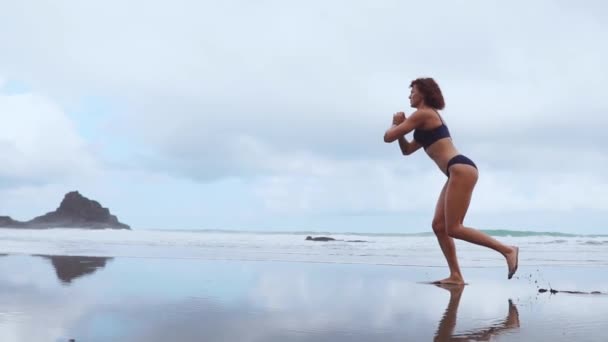 A lo largo del océano, las mujeres ejercitantes realizan embestidas alternando cada pierna en el fondo de rocas y agua. Entrenamiento para bajar de peso durante el resort en la isla — Vídeo de stock