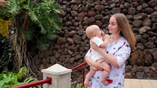 Madre con el niño sonríe y abrazando al bebé hijo sobre la cascada besándose y hablando con él. El concepto de una familia feliz de vacaciones en Canarias — Vídeos de Stock