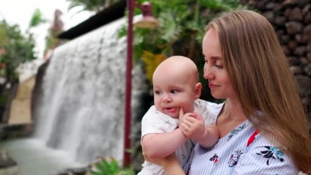 Mutter mit Kind lächelt und umarmt kleinen Sohn über Wasserfall küssen und mit ihm reden. das Konzept einer glücklichen Familie auf einer Reise — Stockvideo