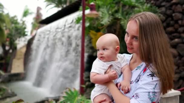 Mutter mit Kind lächelt und umarmt kleinen Sohn über Wasserfall küssen und mit ihm reden. das Konzept einer glücklichen Familie — Stockvideo
