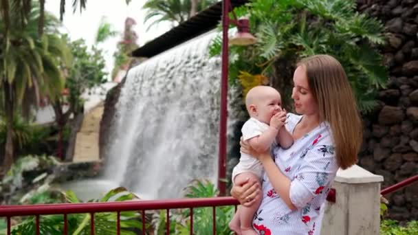 Mor med barn leenden och omfamnande baby son om vattenfall kyssar och prata med honom. — Stockvideo