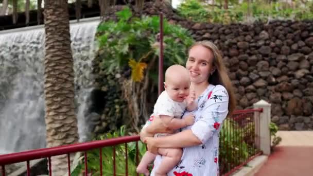 Madre con el niño sonríe y abrazando al bebé hijo sobre la cascada besándose y hablando con él. El concepto de una familia feliz de vacaciones en Canarias — Vídeos de Stock