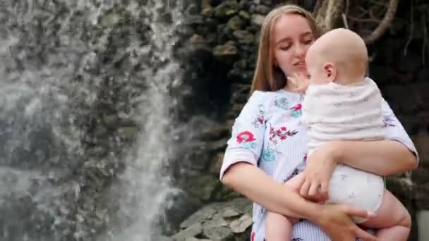 Mutter mit Kind lächelt und umarmt kleinen Sohn über Wasserfall küssen und mit ihm reden. — Stockvideo
