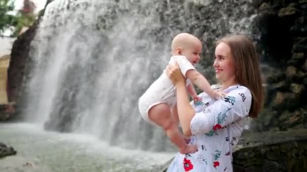 Мать с ребенком улыбается и обнимает маленького сына о том, что водопад целуется и разговаривает с ним. Концепция счастливой семьи в путешествии — стоковое видео