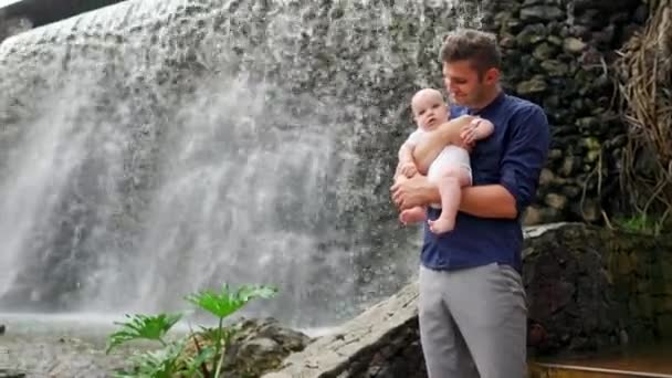 Familie-uitstapje naar de natuur: vader en een meisje van de baby kijken naar de waterval in het regenachtige forest in de zomer — Stockvideo