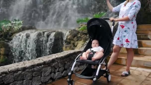 Una giovane madre che cammina con il suo bambino vicino alla cascata scatta foto sul suo smartphone mentre viaggia con la sua famiglia . — Video Stock