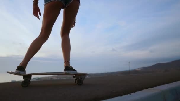 Menina em um passeio de skate na estrada contra a rocha e o céu durante o pôr do sol — Vídeo de Stock