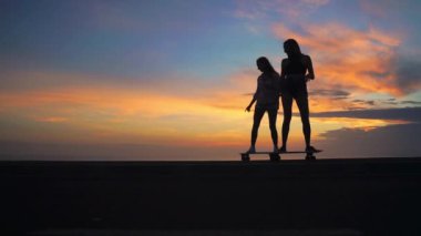 iki arkadaş güzel gökyüzüne yükselen güneşin karşı yamacında kaykay binmek. Ağır çekim 120 fps.