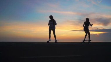 Gökyüzü ve güneş karşı iki kız kaykay silüeti