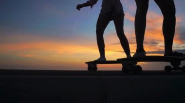 İki kız kız şort ve spor ayakkabılar bacaklar Close-up güzel gökyüzüne yükselen güneşin karşı yamacında kaykay binmek. Ağır çekim 120 fps