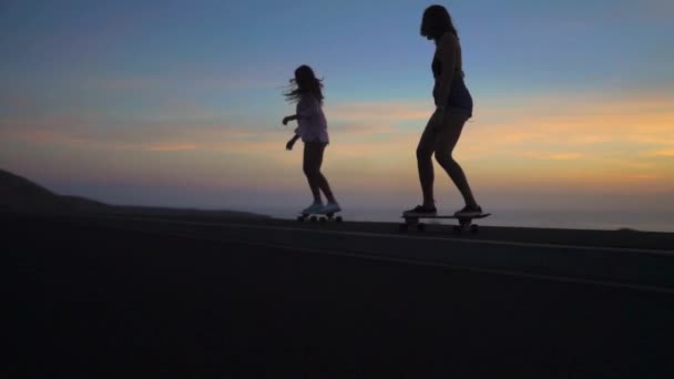 Sziluettjét a lányok egy gördeszka lovagol az úton, a rock és a naplemente gyönyörű ég ellen. A fényképezőgép van-ban jelet ad — Stock videók