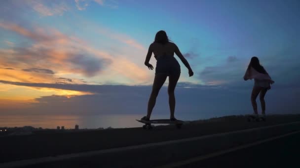 Sylwetka dziewcząt na deskorolce jazda na drodze przed skały i niebo piękna o zachodzie słońca. Aparat jest w ruchu — Wideo stockowe