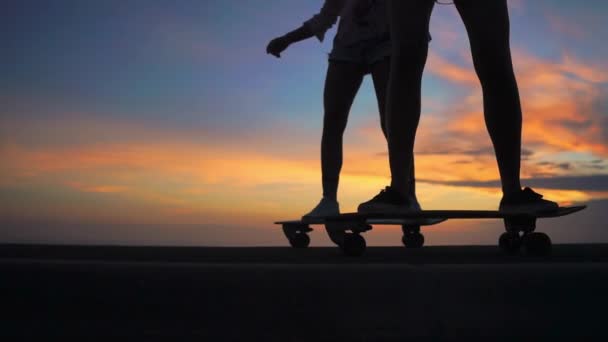 Close-up of the legs of two girls girlfriend in shorts and sneakers ride skateboards on the slope against the beautiful sky of the rising sun. Slow motion 120 fps — Stock Video