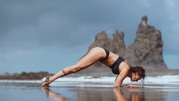 Fille faisant du yoga sur la rive de l'océan sur la plage debout dans un pont de pose sur ses mains. Exercices d'étirement et de relaxation gymnastique — Video