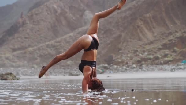 Chica haciendo yoga en la orilla del océano en la playa de pie en un equilibrador de pie en sus manos y estar en reposo y armonía — Vídeo de stock