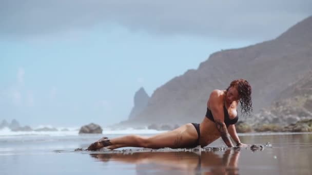 Menina fazendo ioga na margem do oceano na praia de pé em uma ponte de pose em suas mãos. Exercícios de alongamento e relaxamento ginástica. Livre circulação senta-se no fio — Vídeo de Stock