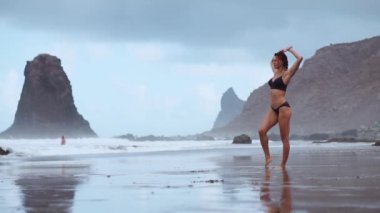 Güzel bir kadın ile siyah volkanik kum okyanus plaj jimnastik egzersizleri pratik bir sağlıklı yaşam tarzı ve açık eğitim gerçekleştirir. Fitness eğitimi