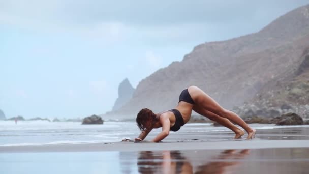 슬림 금발 소녀는 수영복에 큰 검은 헤드폰에 바다의 다가오는 파도에 해안 열 대 해변에서 춤을 음악 청취 — 비디오