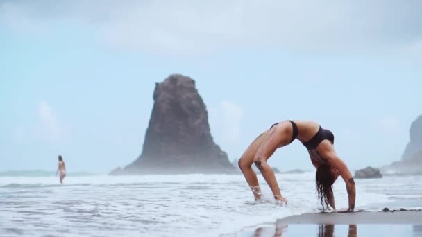 Девушка, занимающаяся йогой на берегу океана на пляже, стоит в позе моста на руках — стоковое видео